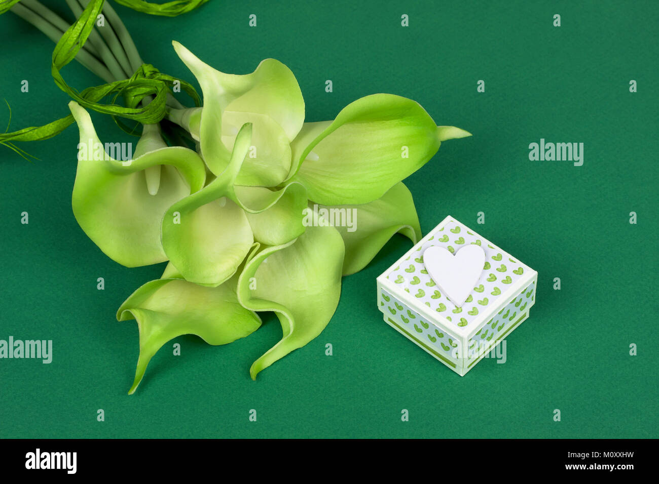 Bouquet de lis calla jaune vert avec boîte cadeau et coeur blanc sur fond de carton vert Banque D'Images