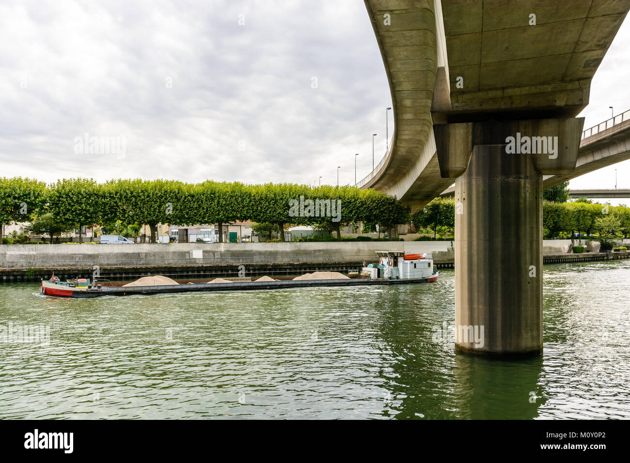 Un chaland chargé de marchandises sèches en vrac avec du gravier à la tête de la marne dans la banlieue de Paris, en passant sous les rampes de l'autoroute A86. Banque D'Images