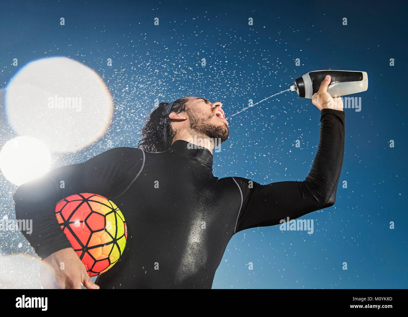 Hispanic man holding soccer ball pulvériser de l'eau dans la bouche Banque D'Images