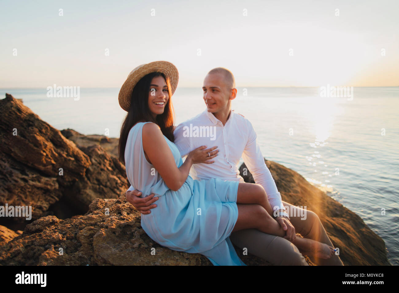 Couple assis sur des rochers sur la plage au coucher du soleil Banque D'Images