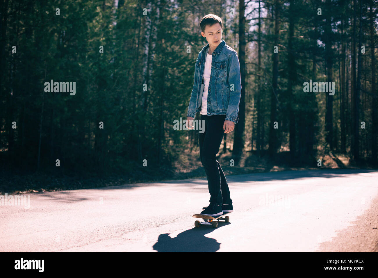 Caucasian man skateboarding sur route près de la forêt Banque D'Images