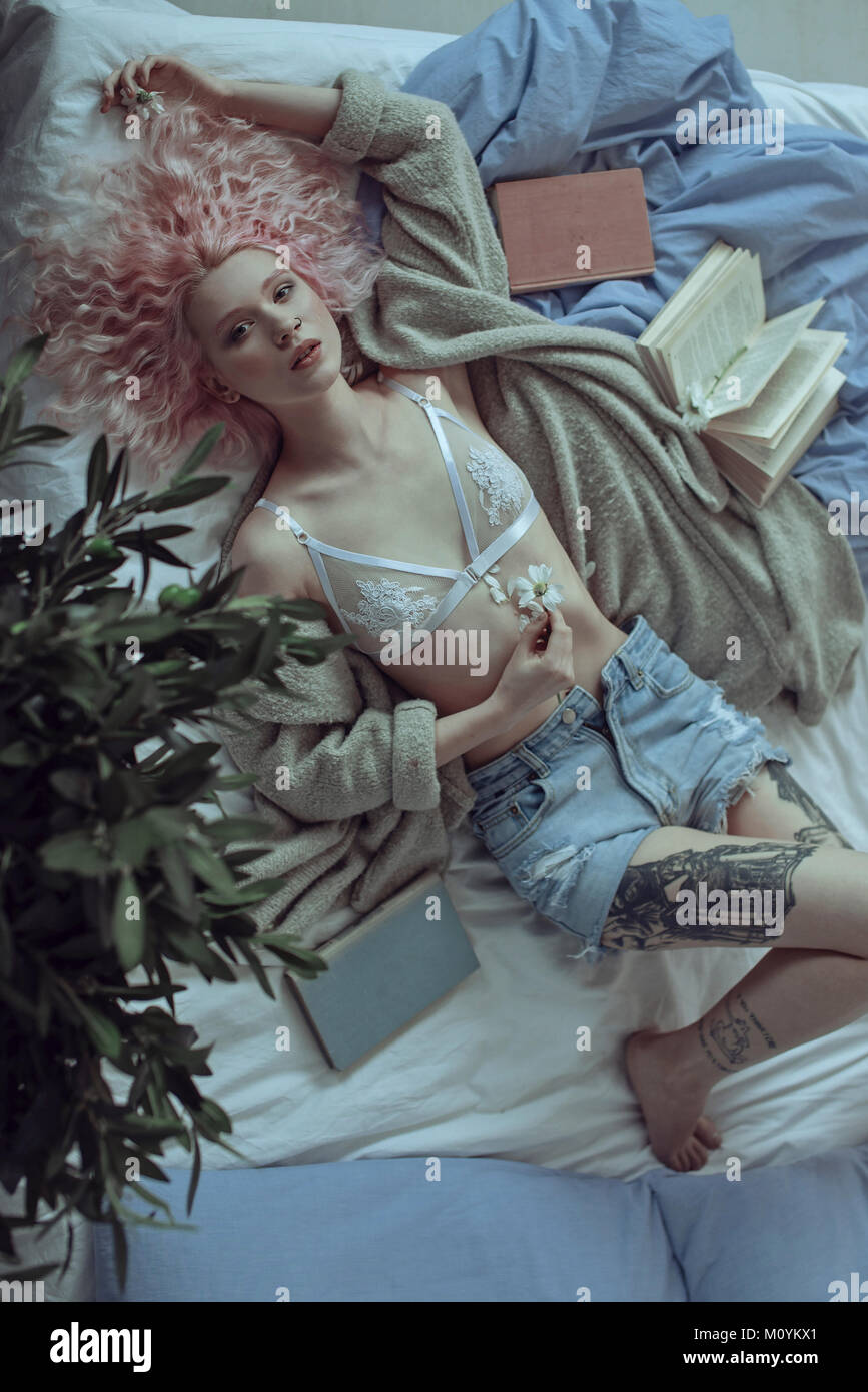 Femme de race blanche aux cheveux roses portant sur bed holding flower Banque D'Images