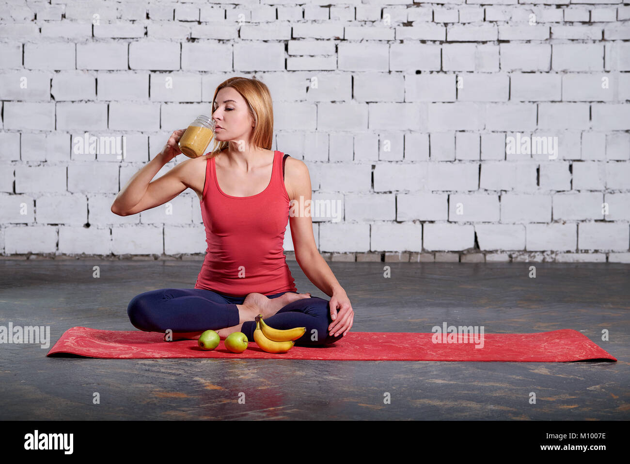 Le yoga le végétarisme. Smoothies boissons fille. Femme ayant une yelloy jus dans la salle après sa pratique du yoga. concept de vie en bonne santé. Banque D'Images