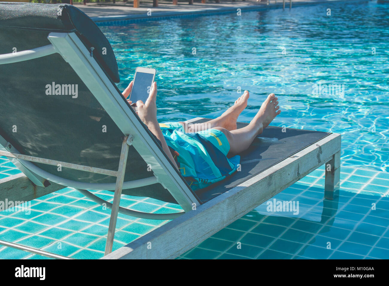 Femme couchée dans un lit et jouer son smartphone à côté de la piscine. Banque D'Images
