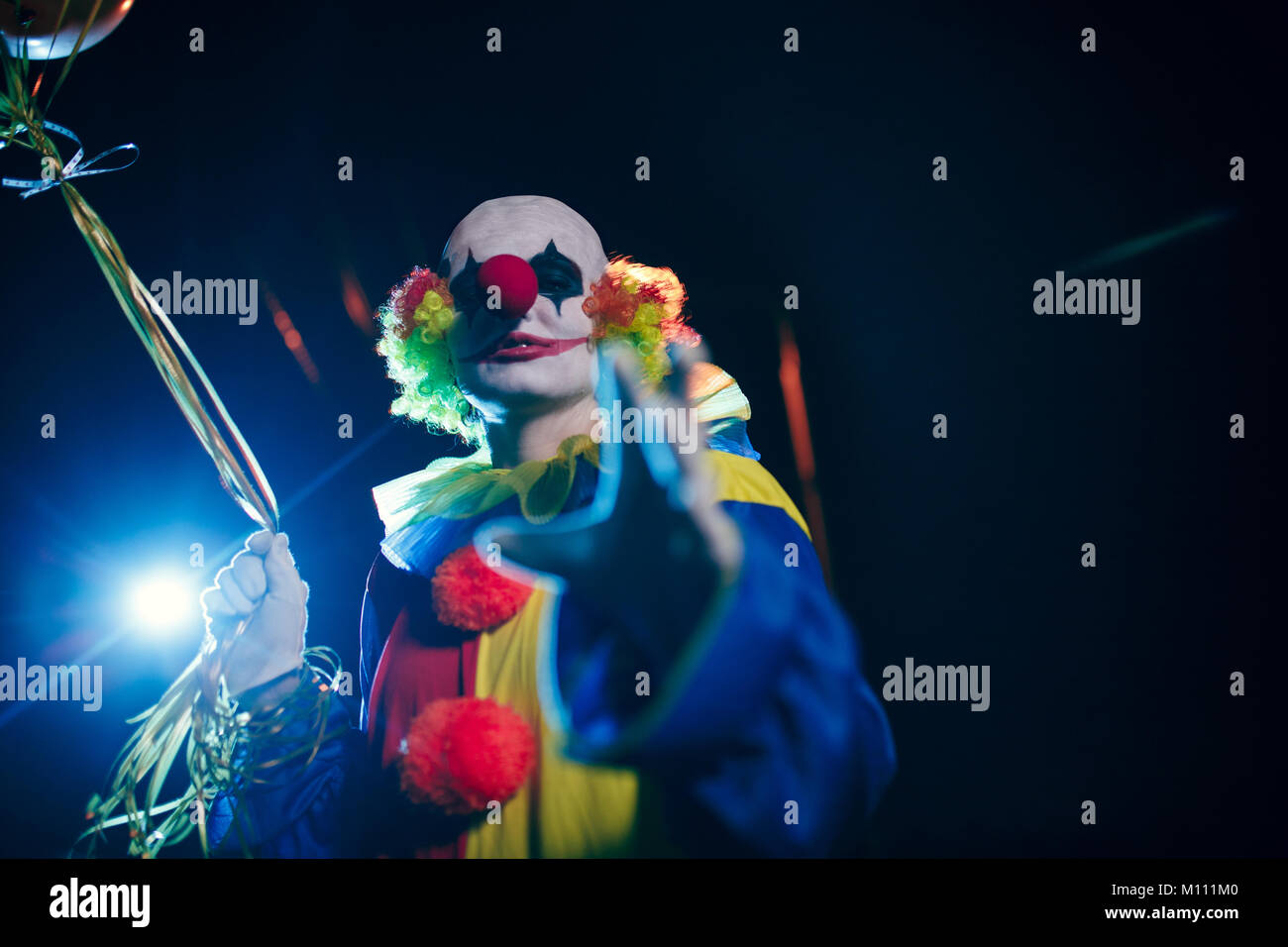 Photo de clown souriant avec des ballons contre l'arrière-plan de brûler la nuit sur la rue lanterne Banque D'Images