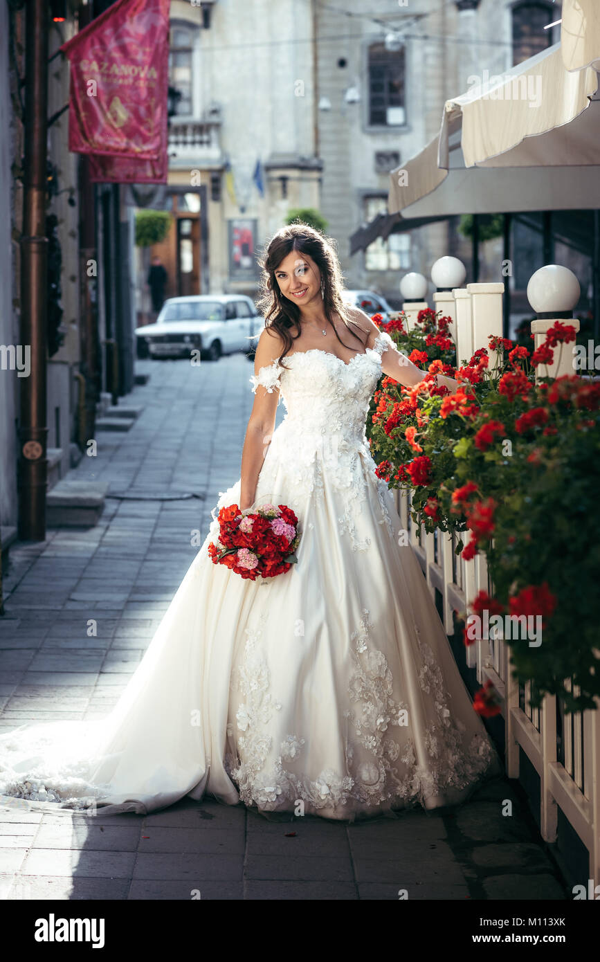 Portrait en pied de la belle brune à long mariée robe de mariage tenant le  bouquet de mariage rose et rouge dans la rue Photo Stock - Alamy
