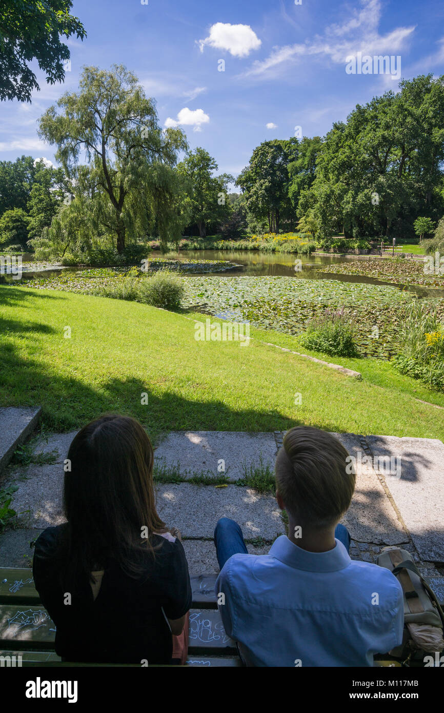 Jeune couple à l'arrière assis ensemble sur un banc à l'ombre. Banque D'Images