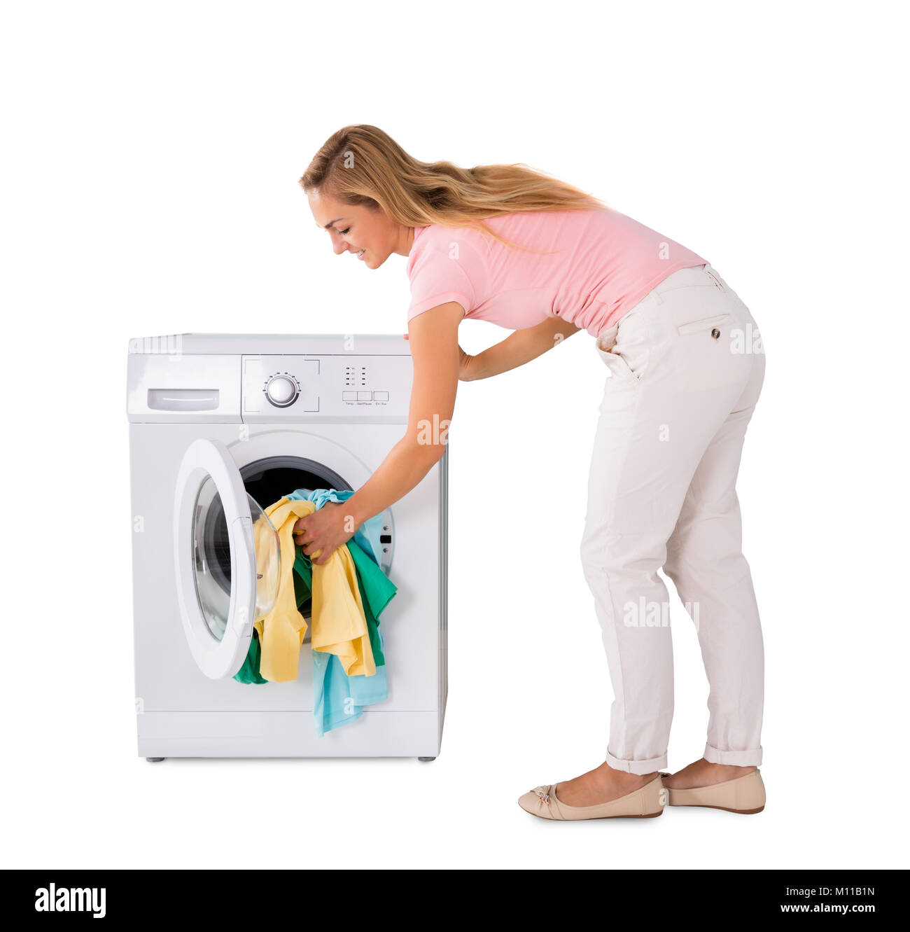 Smiling Young Woman Putting blanchisserie dans un lave-linge contre fond blanc Banque D'Images