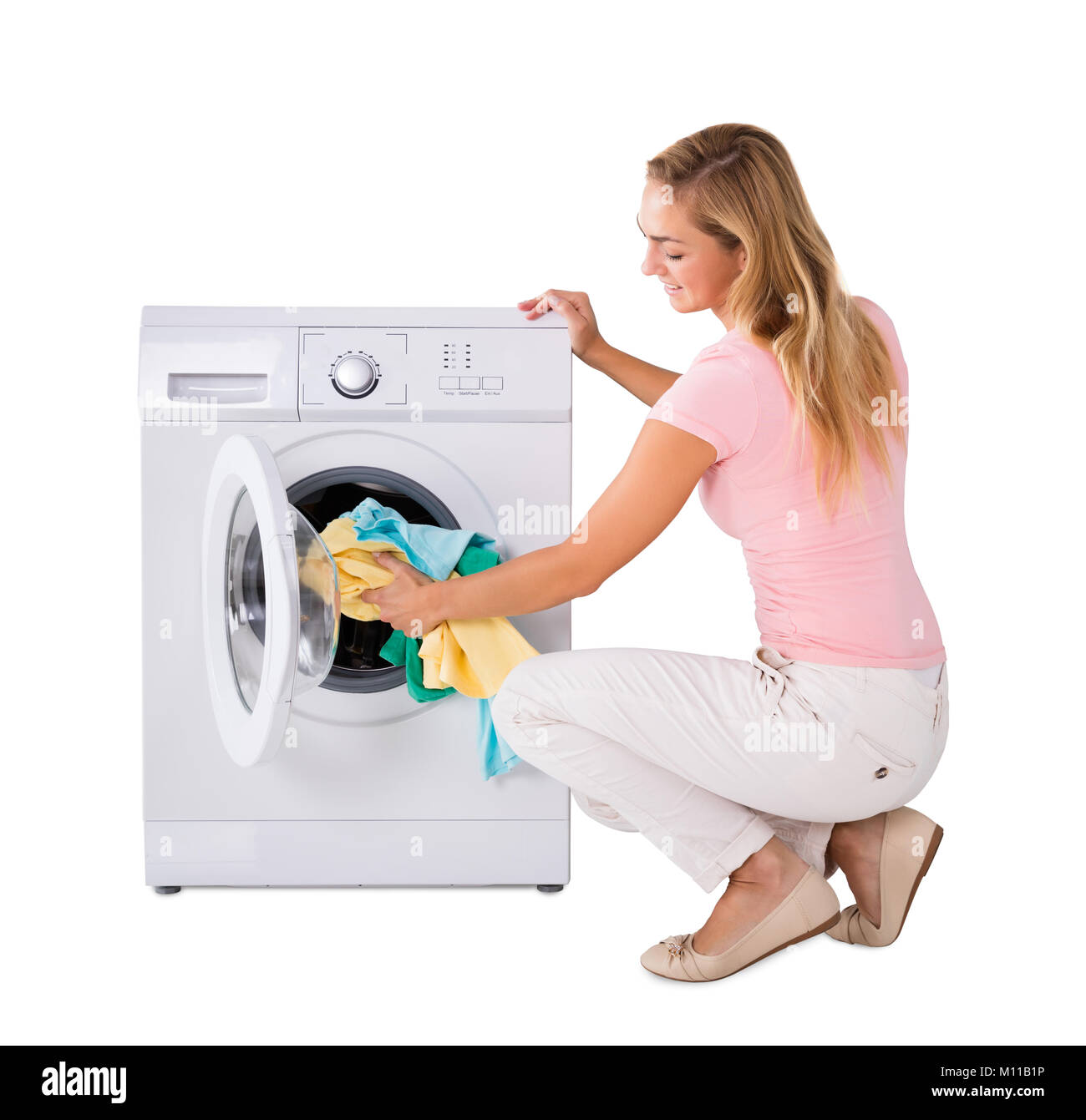 Smiling Young Woman Putting blanchisserie dans un lave-linge contre fond blanc Banque D'Images