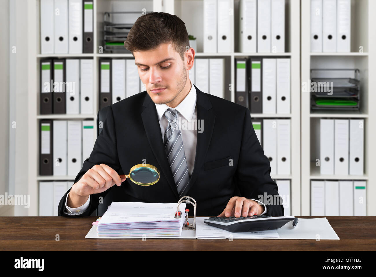 Jeune homme d'analyser le projet de loi avec une loupe sur le lieu de travail Banque D'Images