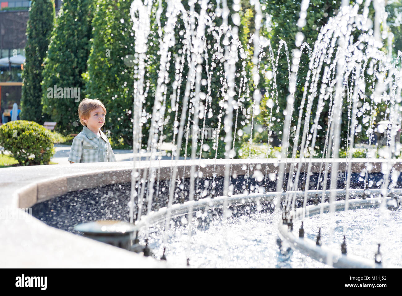 Enfant de trois ans dans le parc avec fontaine à eau et ciel bleu Banque D'Images