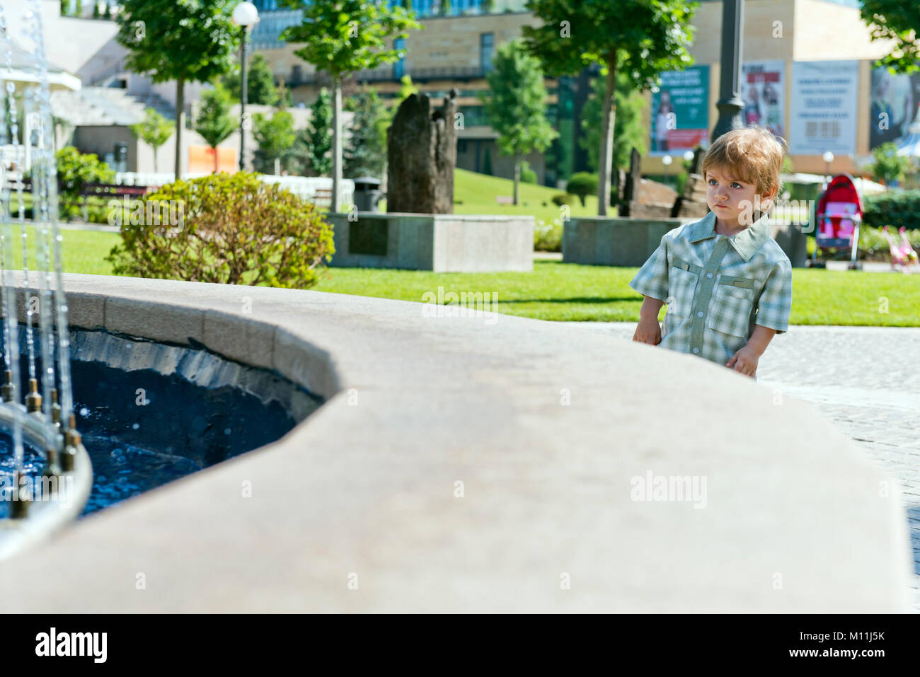 Enfant de trois ans dans le parc avec fontaine à eau et ciel bleu Banque D'Images