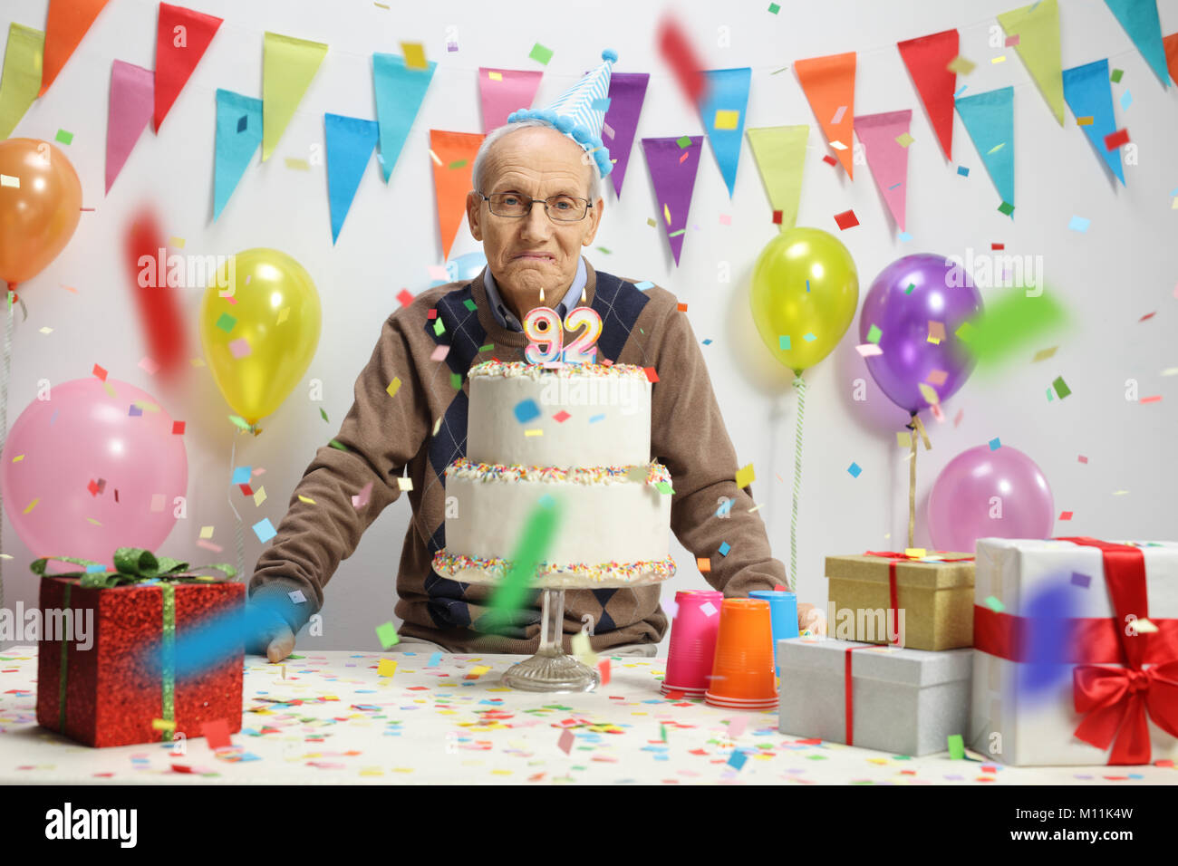 Triste homme âgé avec un gâteau d'anniversaire contre un mur avec décorations Banque D'Images