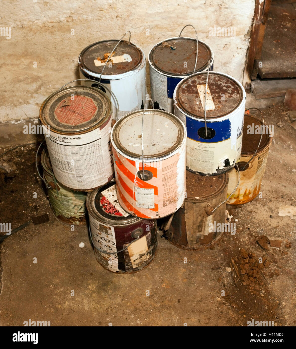 Contenants de peinture vides empilées sur le plancher du sous-sol sale. Banque D'Images