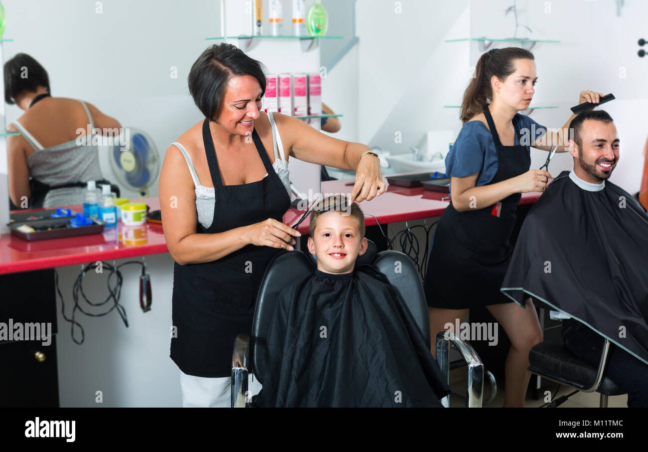 Cheerful woman coiffure dans la coupe de cheveux de l'aire d'heureux garçon 7-9 ans dans des instituts de beauté Banque D'Images