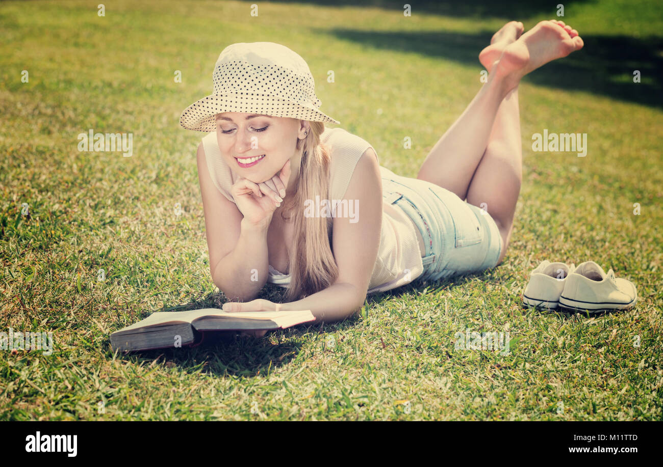 Portrait of young Beautiful woman lying on pelouse verte dans le parc et la lecture de livre sur la journée d'été Banque D'Images