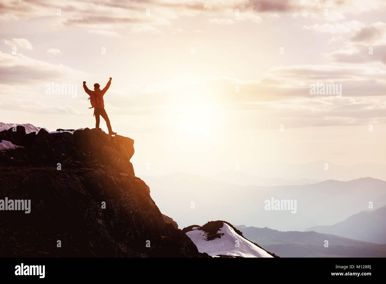 L'homme à poser au sommet de montagne gagnant contre les montagnes et le coucher du soleil Banque D'Images