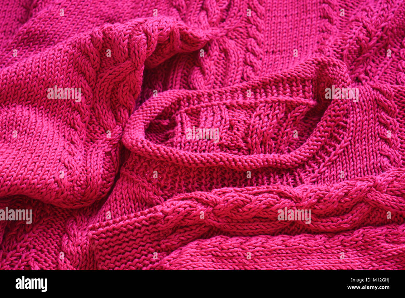 La main à la main, de couleur rose vif en tricot pull en coton avec un câble unique. Banque D'Images