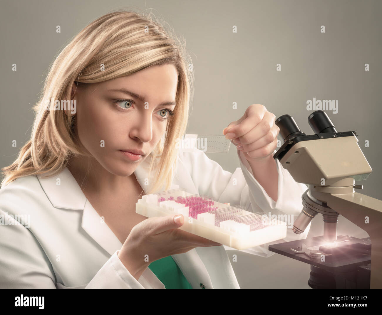 Jeune femme microscopiste à manteau blanc sélectionne un échantillon de tissu pour analyse au microscope. Cette image est tonique. Banque D'Images