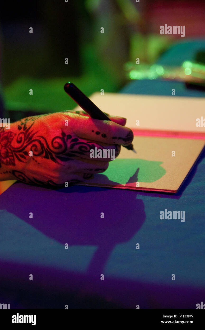 Une femme de la main de henné est prêt à écrire sur une feuille de papier d'ordinateur portable avec des ombres vertes et rouges sur la page. Banque D'Images
