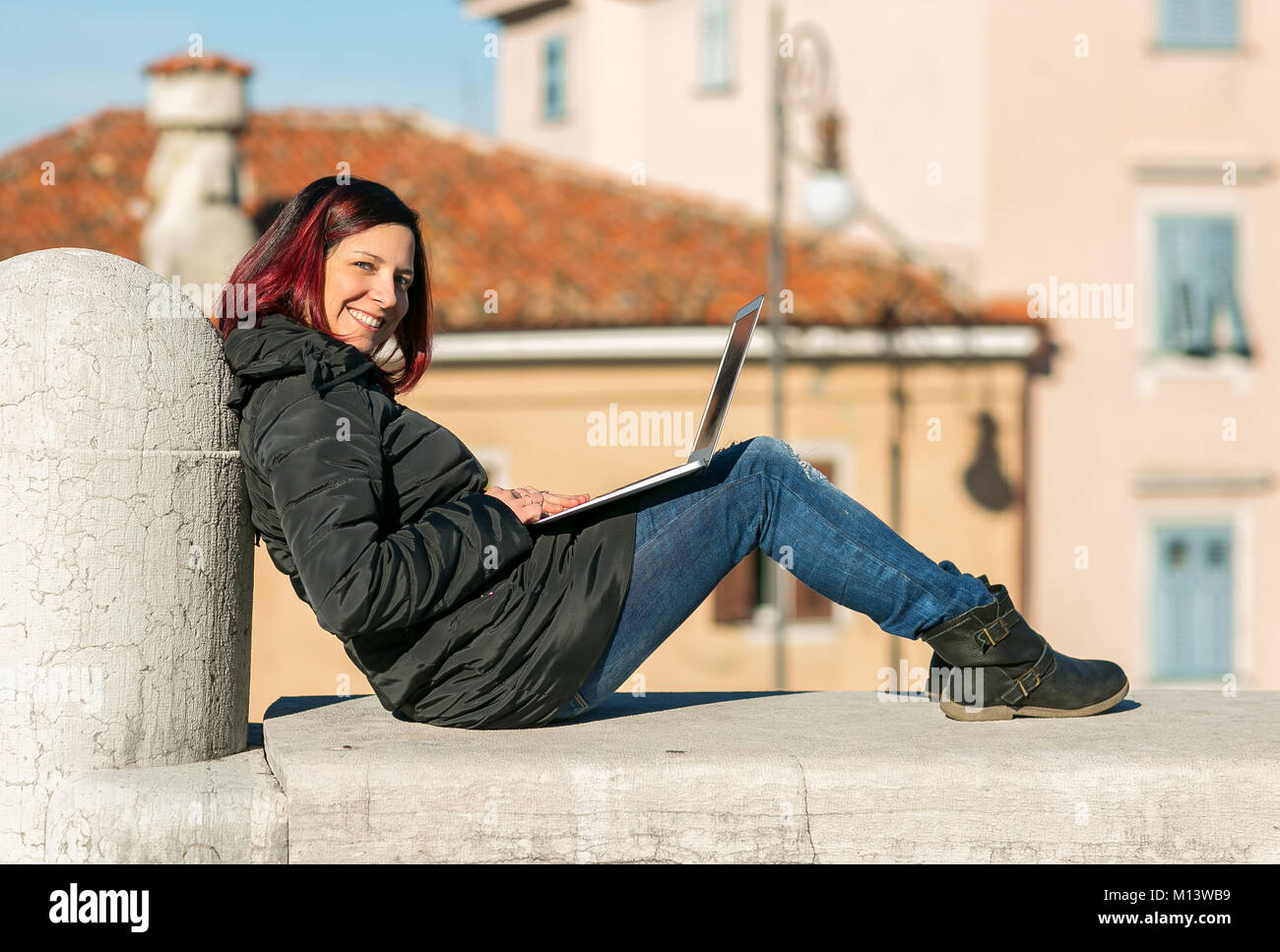 Heureux souriant beau rousse jeune femme assise sur un petit mur et de travailler sur un ordinateur portable - Notion de détente dans la nature. Banque D'Images