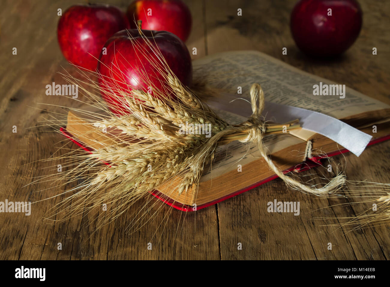 Des pommes rouges et des épis de blé sur le livre sur une table de bois sur un arrière-plan flou Banque D'Images