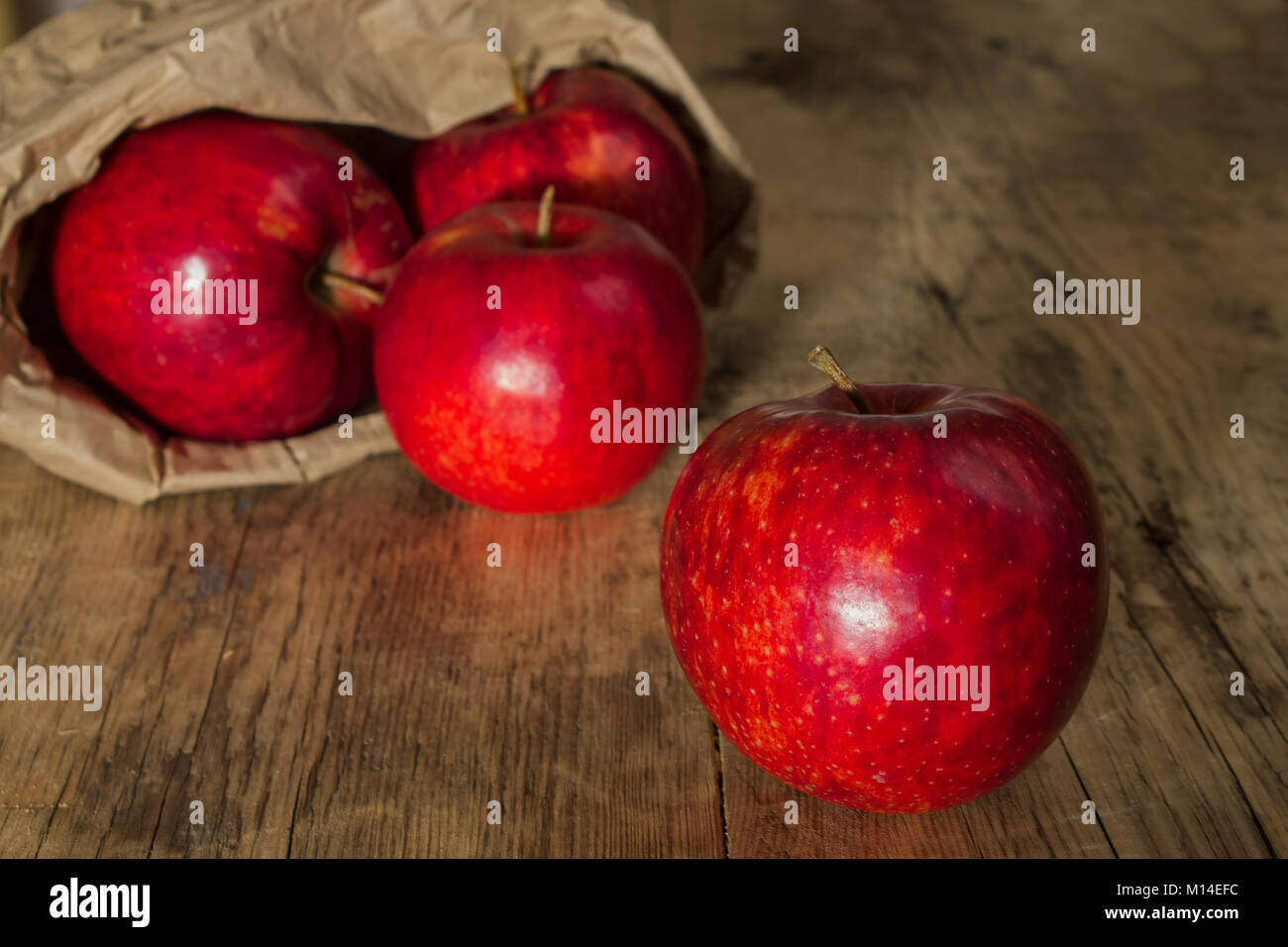 Pomme Rouge juteuse sur un fond de bois sur un arrière-plan flou sac de papier avec des pommes Banque D'Images