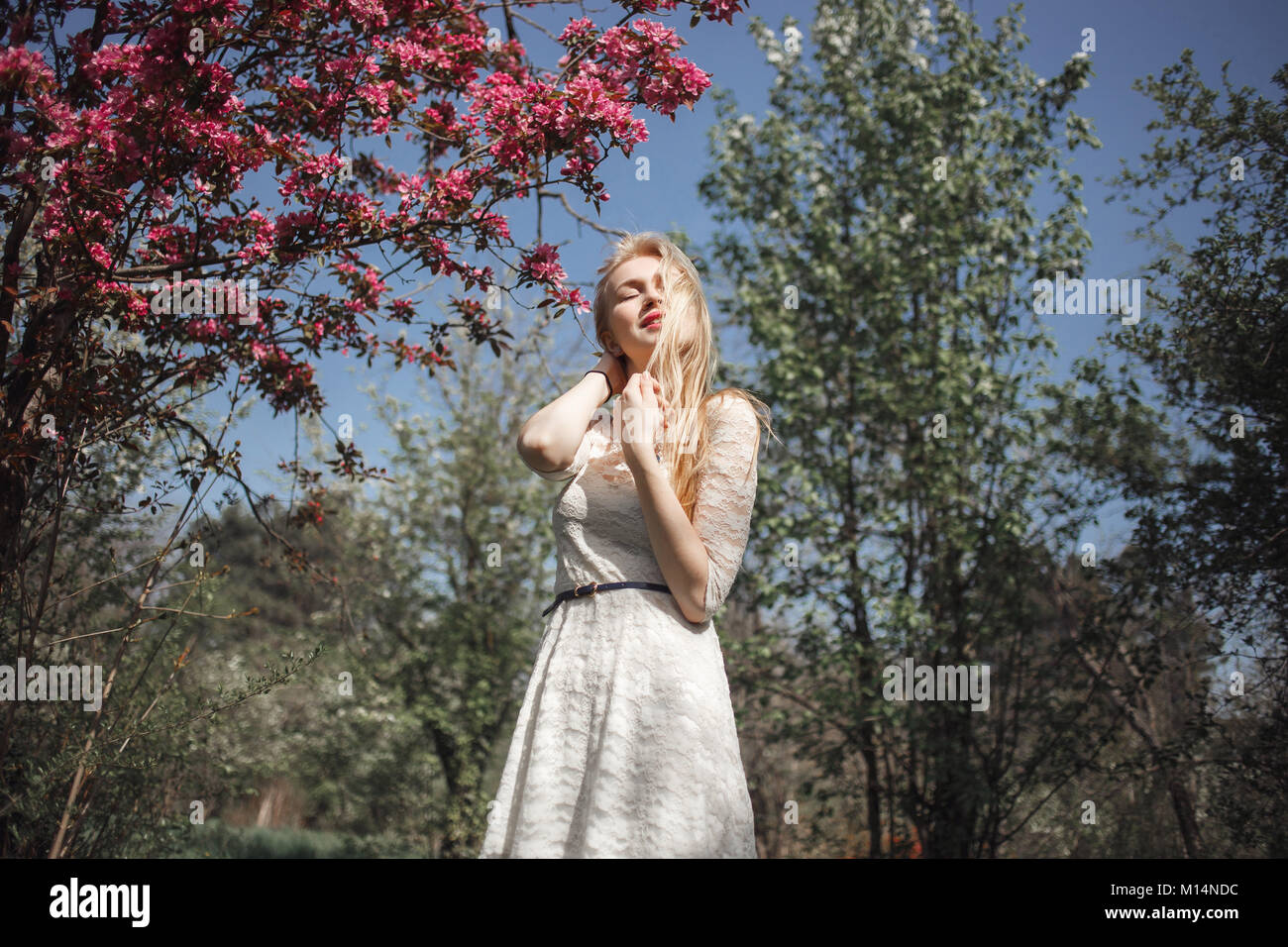Belle jeune blonde woman enjoying journée ensoleillée dans le parc pendant la saison des cerisiers en fleur sur un beau jour de printemps Banque D'Images
