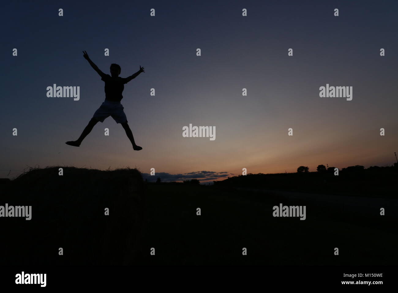 Adolescent mâle sautant en l'air pendant le coucher du soleil. Banque D'Images