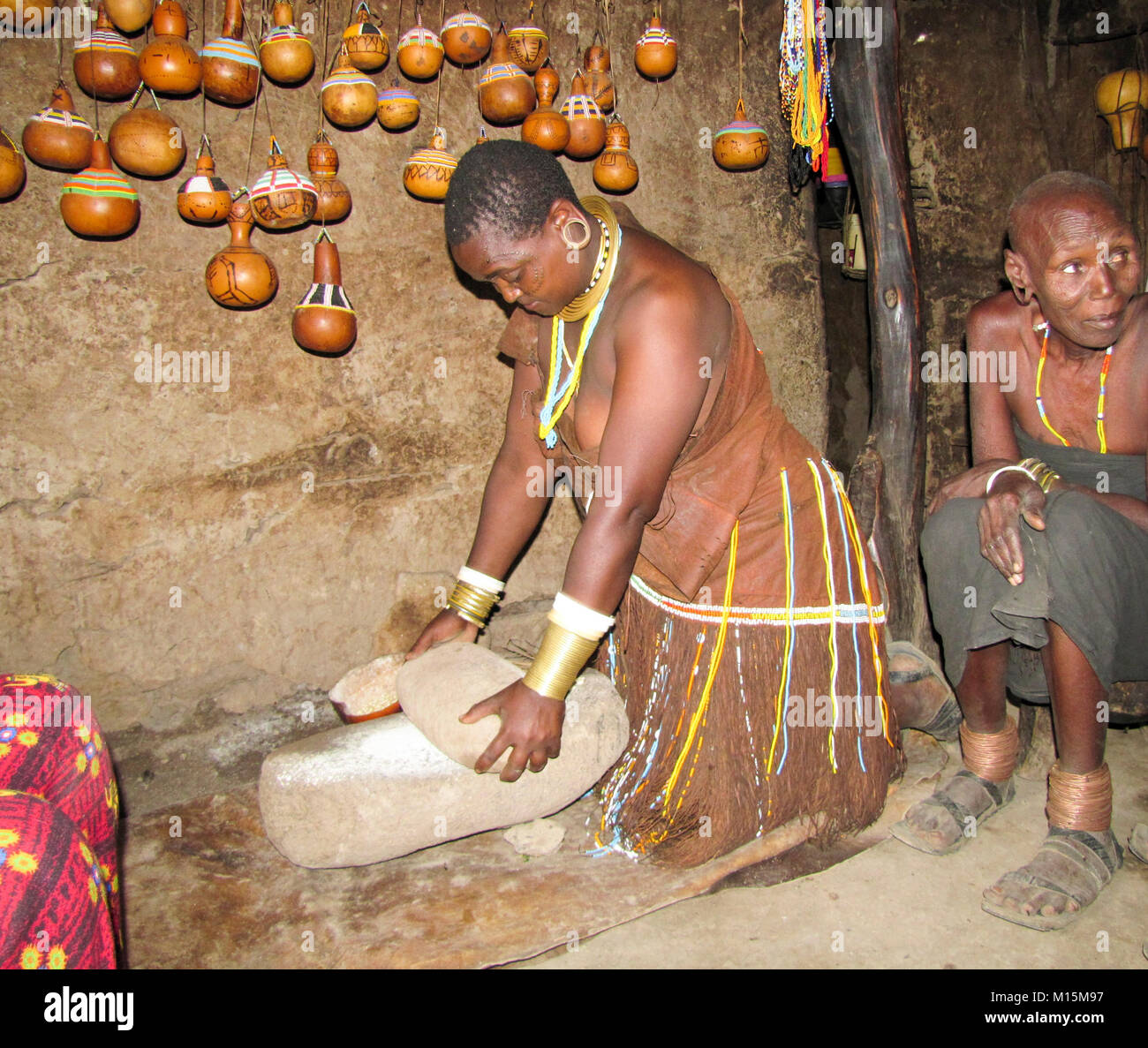 Femme Datoga en cuir traditionnelle robe ornée de perles et de bracelets en laiton la mouture de céréales pour la farine. Banque D'Images