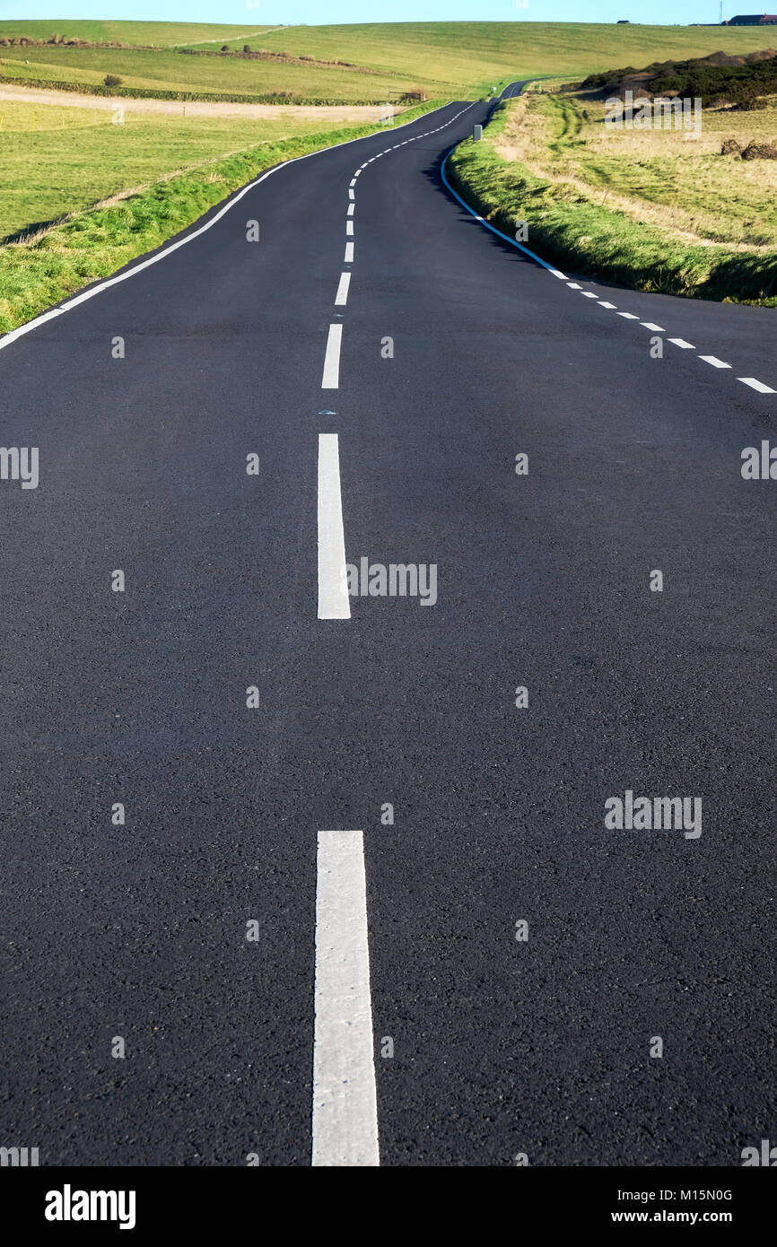 Une route de campagne d'asphalte gris avec des lignes blanches au milieu, le point de vue faible rend la route et des lignes blanches de gros au premier plan menant à Banque D'Images