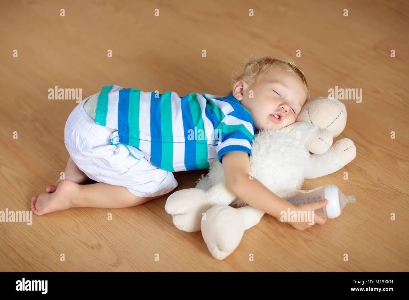 Bébé Dormir Sur Un Plancher En Bois Avec Des Moutons En Peluche Et  Bouteille De Lait. Assez Drôle De Petit Garçon S'endormir De Ramper Sur  Plancher De Bois Franc À La Maison.