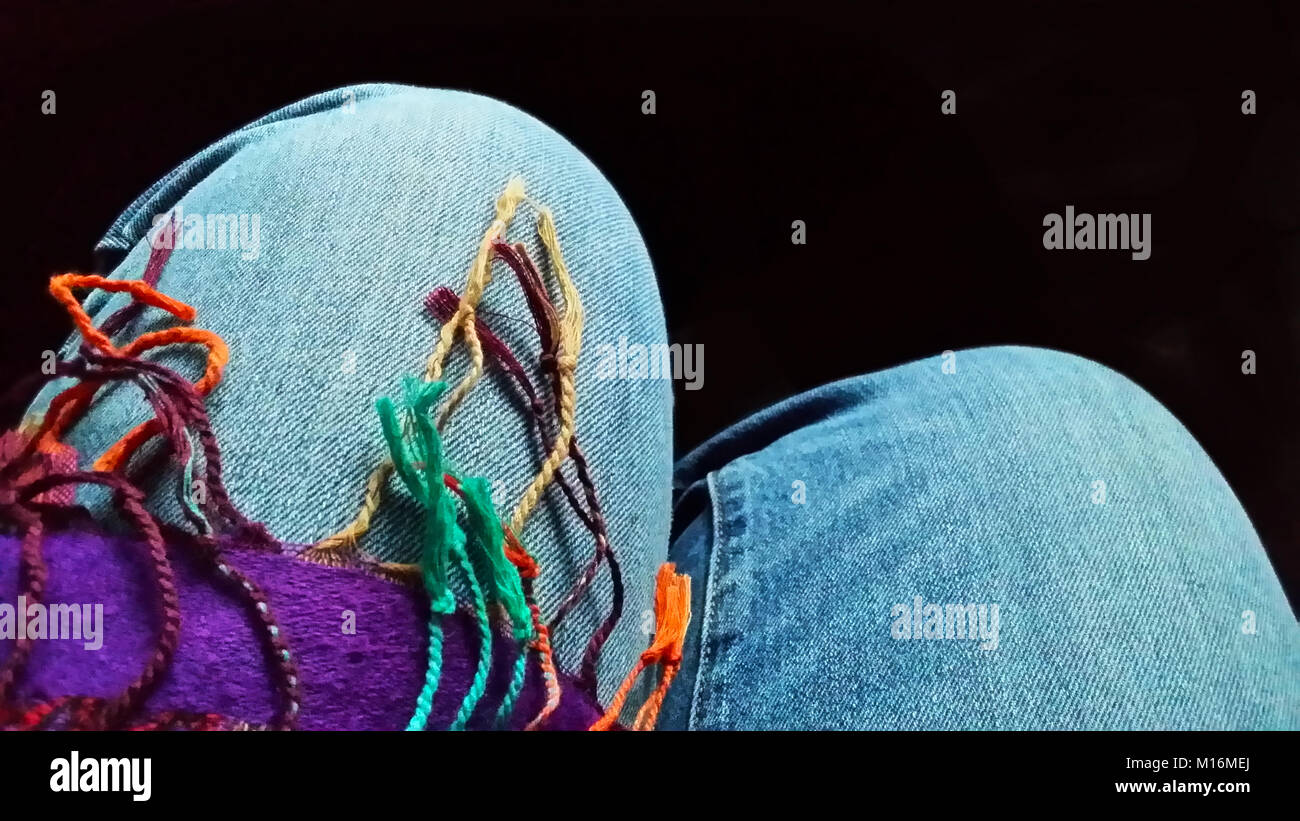 Les jambes - les genoux de femme assise en multipcolor denium jeans drapé de fringe du foulard Banque D'Images