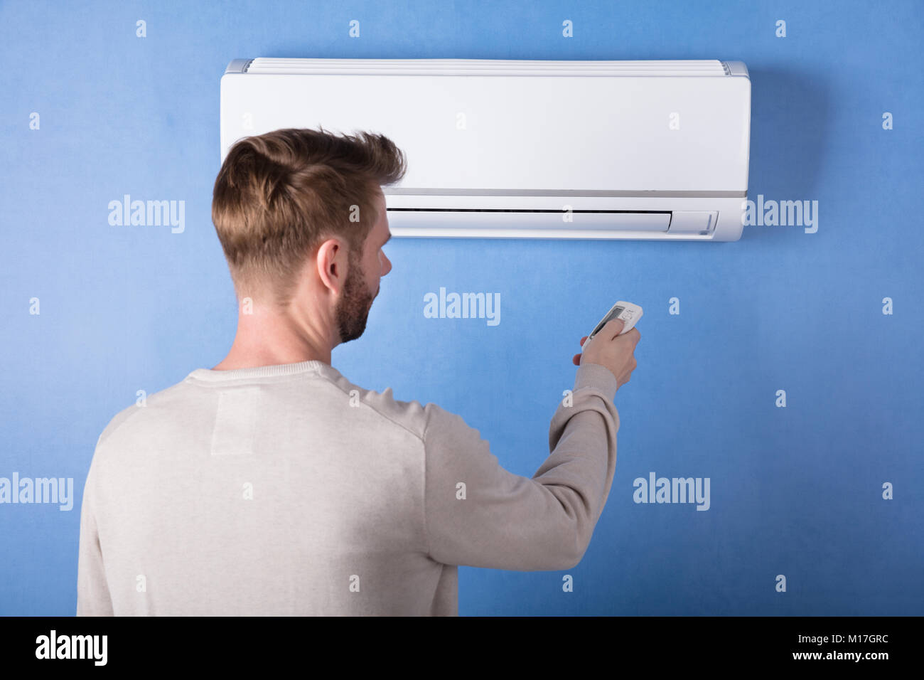 Vue arrière de l'exploitation d'un jeune homme monté sur Climatiseur mural bleu Banque D'Images