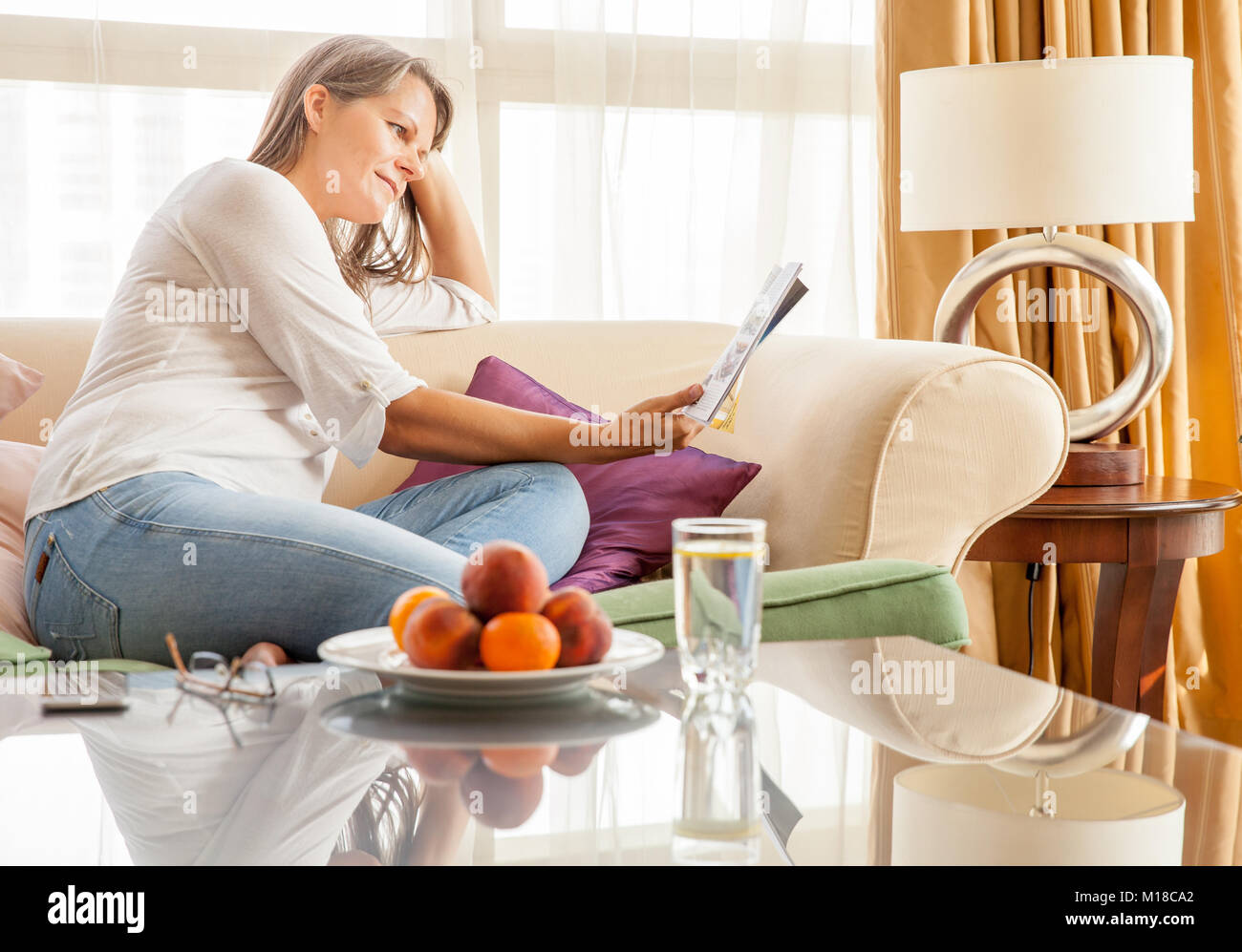 Femme mature est de vous détendre sur un canapé dans son appartement avec un magazine Banque D'Images