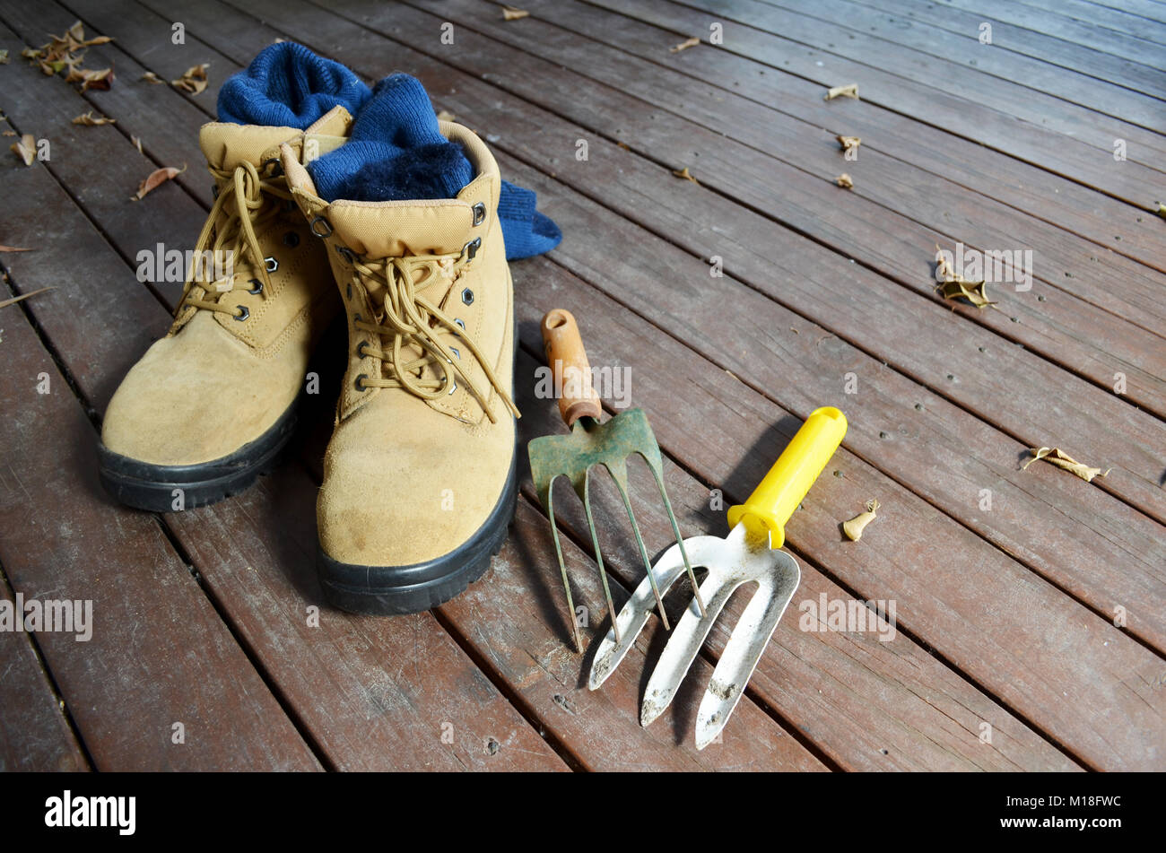 Paire de bottes de travail avec outils de jardin sur une terrasse en bois Banque D'Images