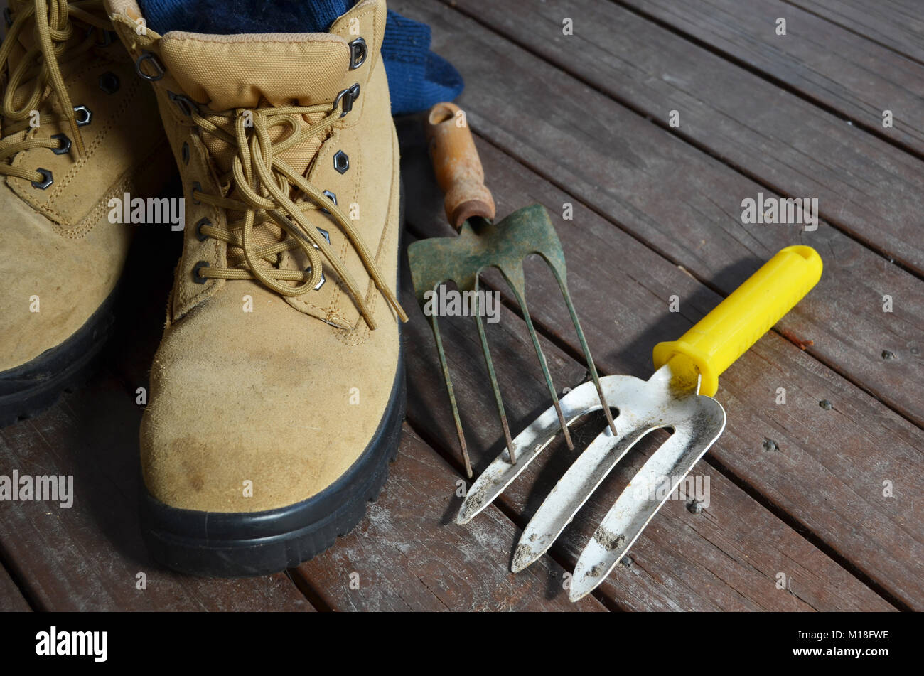 Paire de bottes de travail avec outils de jardin sur une terrasse en bois Banque D'Images