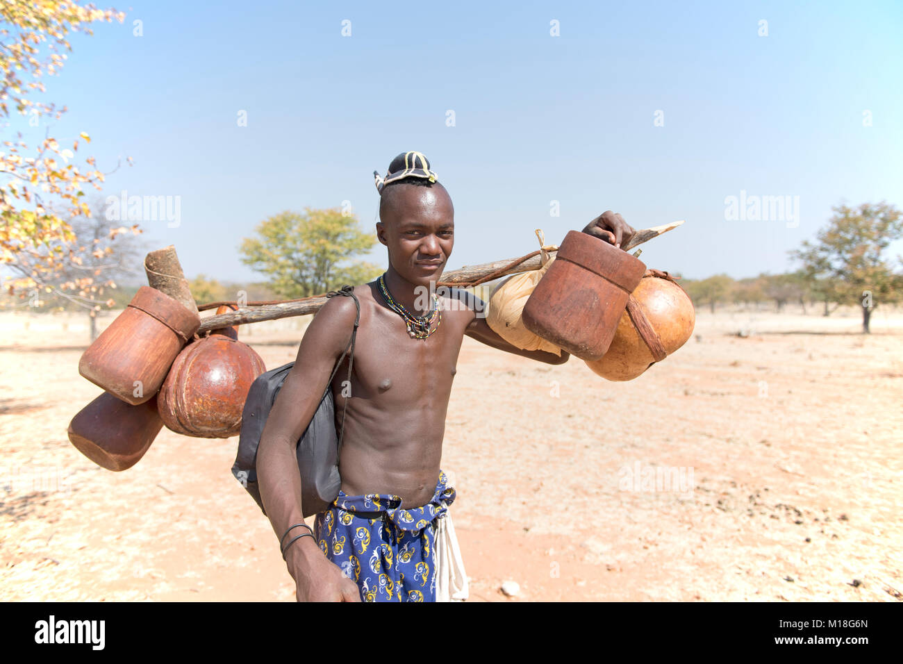 Les jeunes Himbamann porte réservoir d'eau et de la nourriture sur le transport de bétail,Kaokoveld,Namibie Banque D'Images