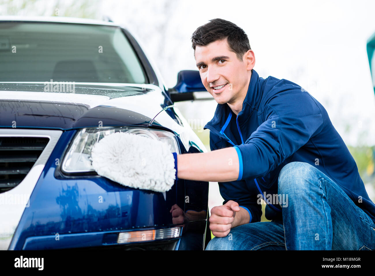 Smiling man Nettoyage du projecteur sur sa voiture Banque D'Images