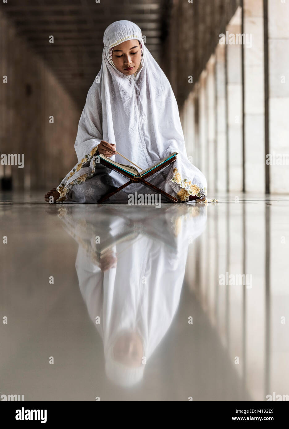 L'Islam girl reading Kuran à l'intérieur de la Mosquée Istiqlal au cours du mois de Ramadan, Jakarta, Indonésie Banque D'Images