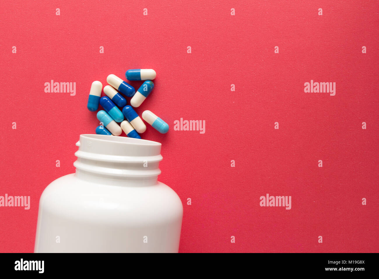 Groupe d'autres comprimés blanc et bleu. Capsules spilling out of white bouteille. Fond rouge. Banque D'Images