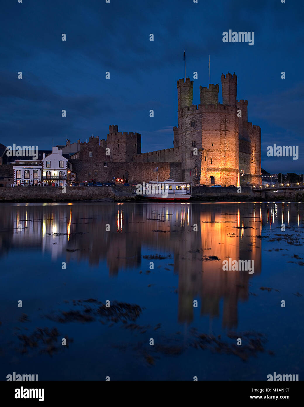 Château de Caernarfon sur la côte nord du Pays de Galles dans la nuit avec des reflets dans la mer Banque D'Images