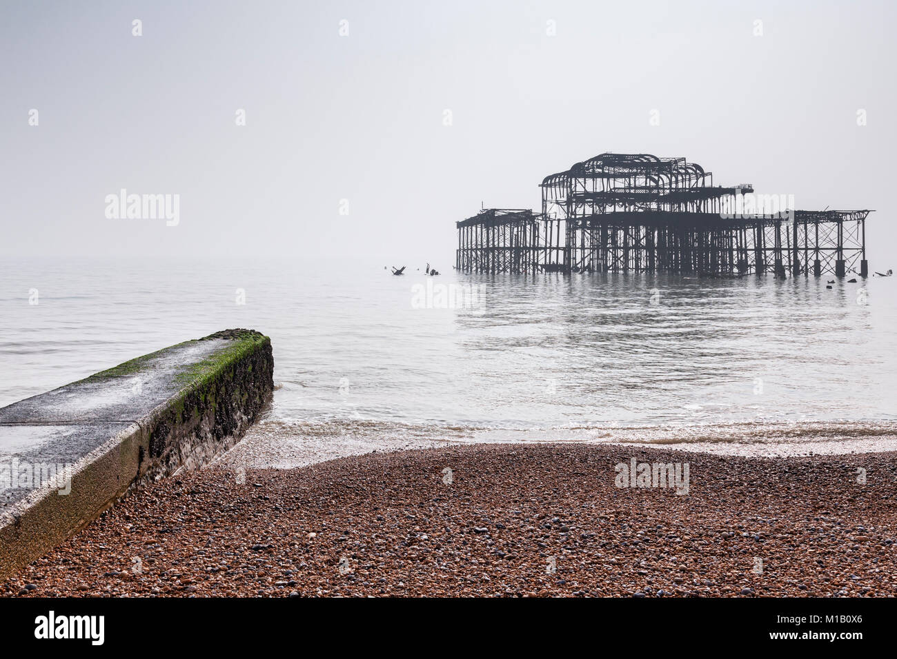 La plage de Brighton et le reste de l'ancienne jetée ouest en un jour brumeux dans télévision lumière, Sussex, England, UK. Banque D'Images