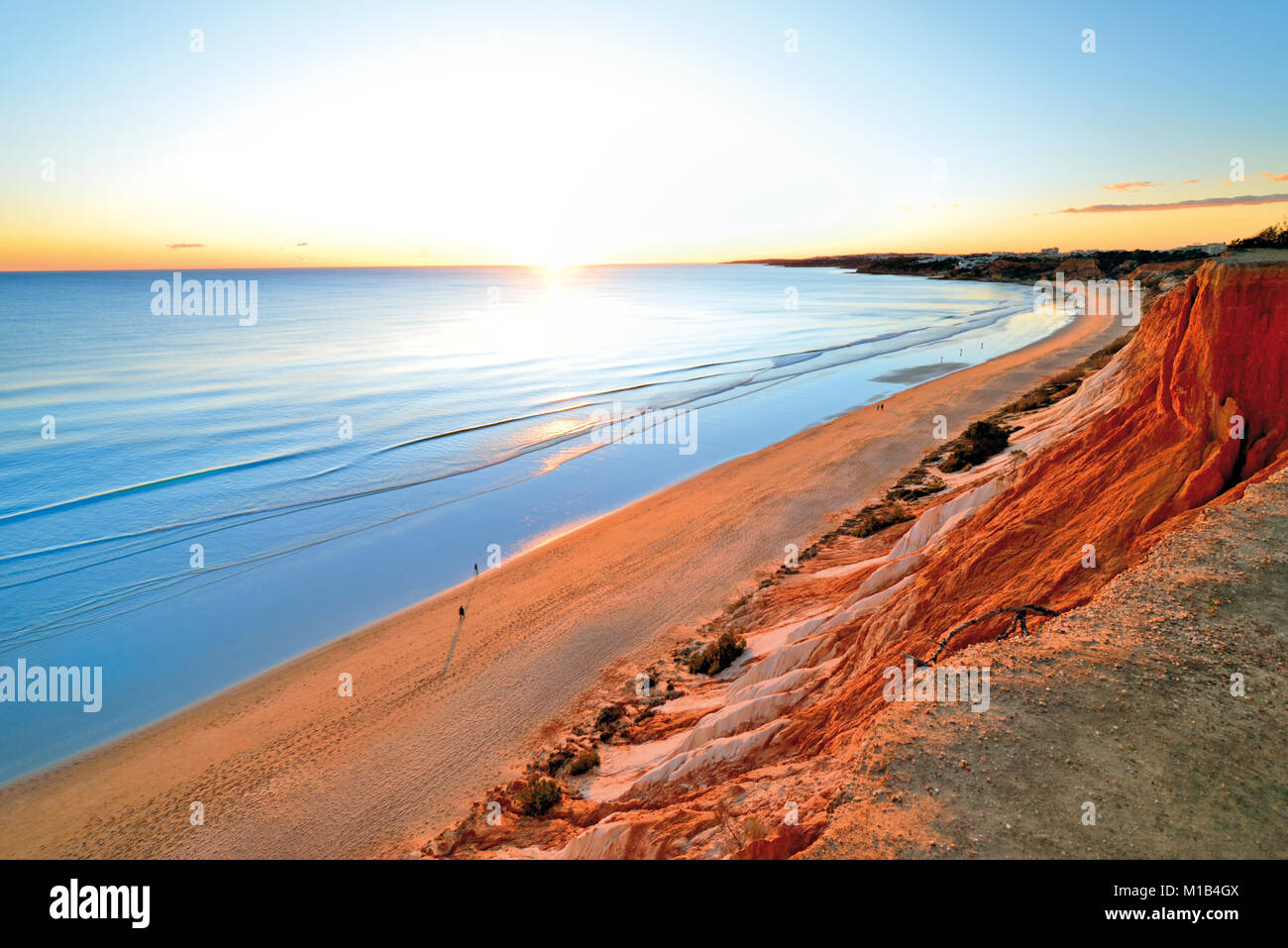 Scenic coucher du soleil à longue plage de sable avec du sable et falaises fissurées océan calme Banque D'Images