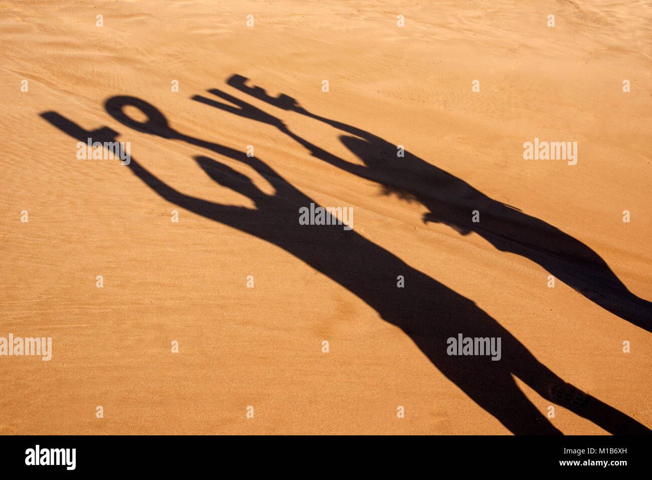 Gros plan de l'ombre d'un homme et une femme tenant quelques lettres formant le mot amour au-dessus de leur tête sur le sable d'une plage Banque D'Images