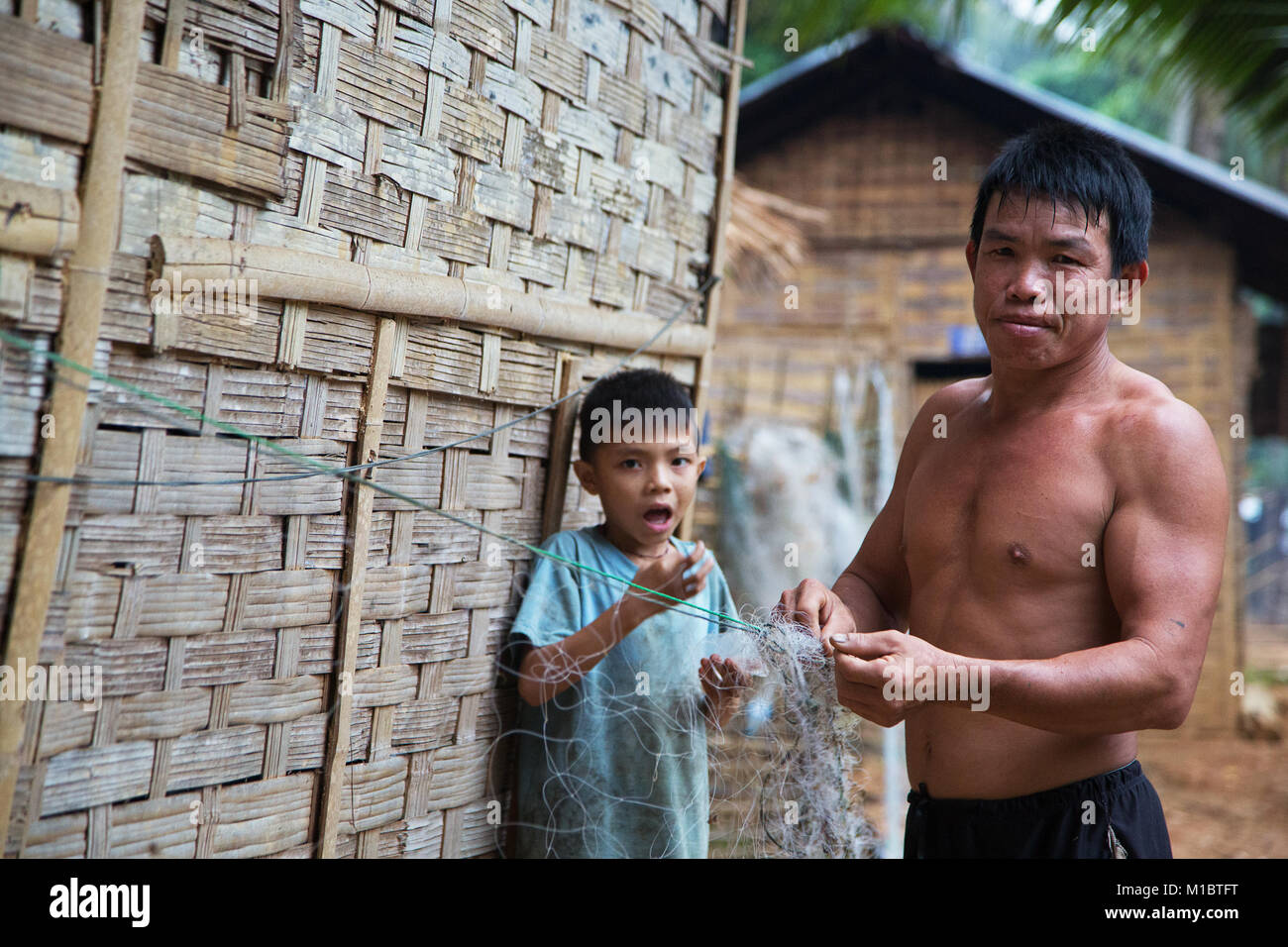 Un pêcheur répare son traditionell net dans un petit village à la rivière Nam Ou pendant que son fils est le regarder, le nord du Laos, Asie Banque D'Images