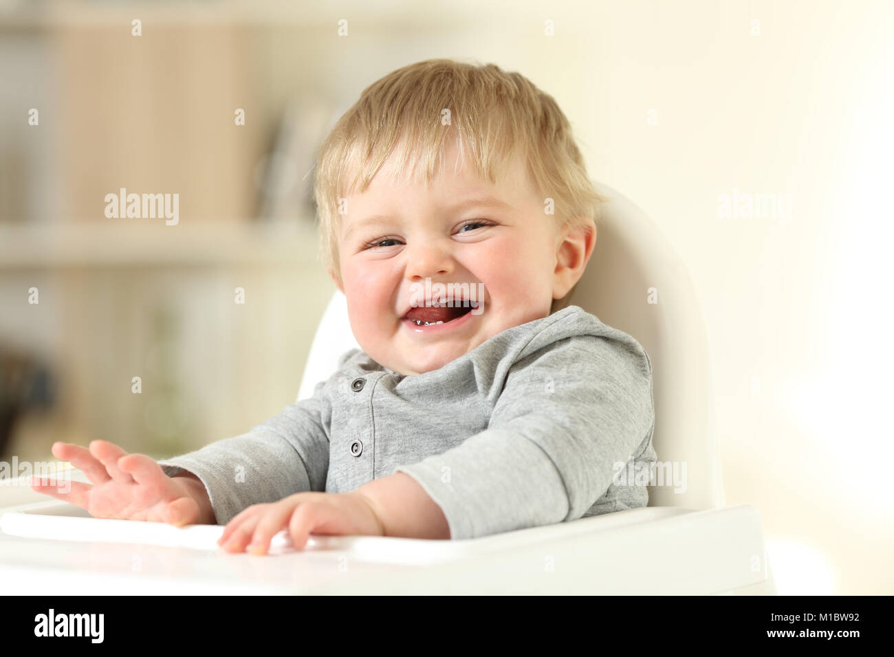 Portrait d'un bébé joyeux avec ses premières dents en vous regardant assis sur une chaise haute Banque D'Images