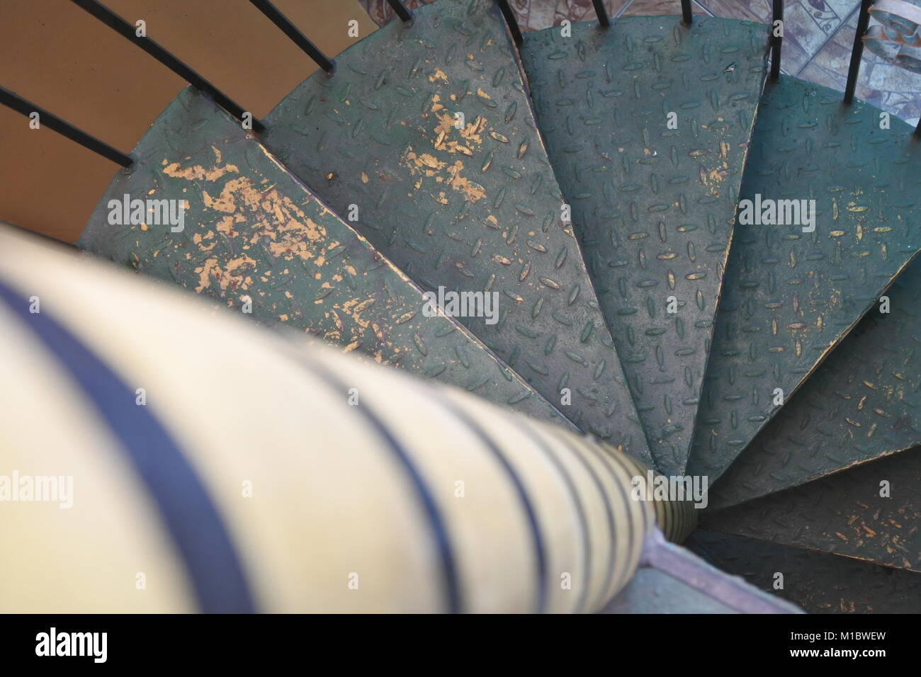 Descendre un escalier en colimaçon vert en métal patiné avec un poteau central noir et jaune faisant écho à sa conception en spirale. Banque D'Images