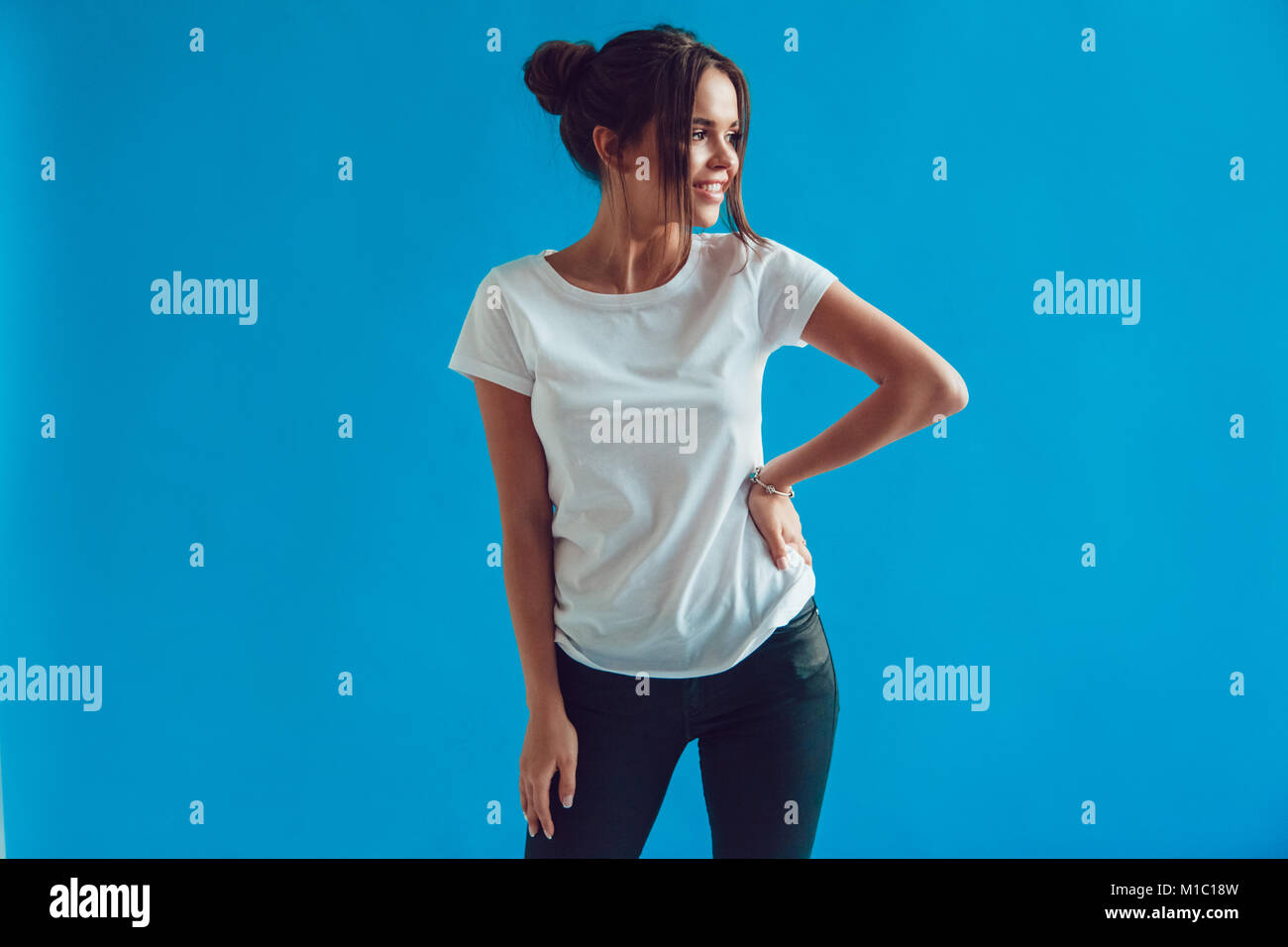 Belle femme dans un t-shirt blanc se dresse sur un fond bleu. Mock-up. Banque D'Images