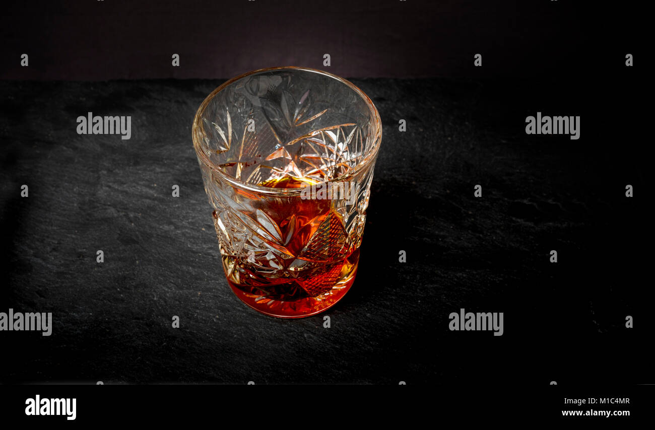 Whisky (ou whisky) dans un verre de cristal de luxe coupe lourd tumbler sur une table en bois avec un arrière-plan foncé Banque D'Images